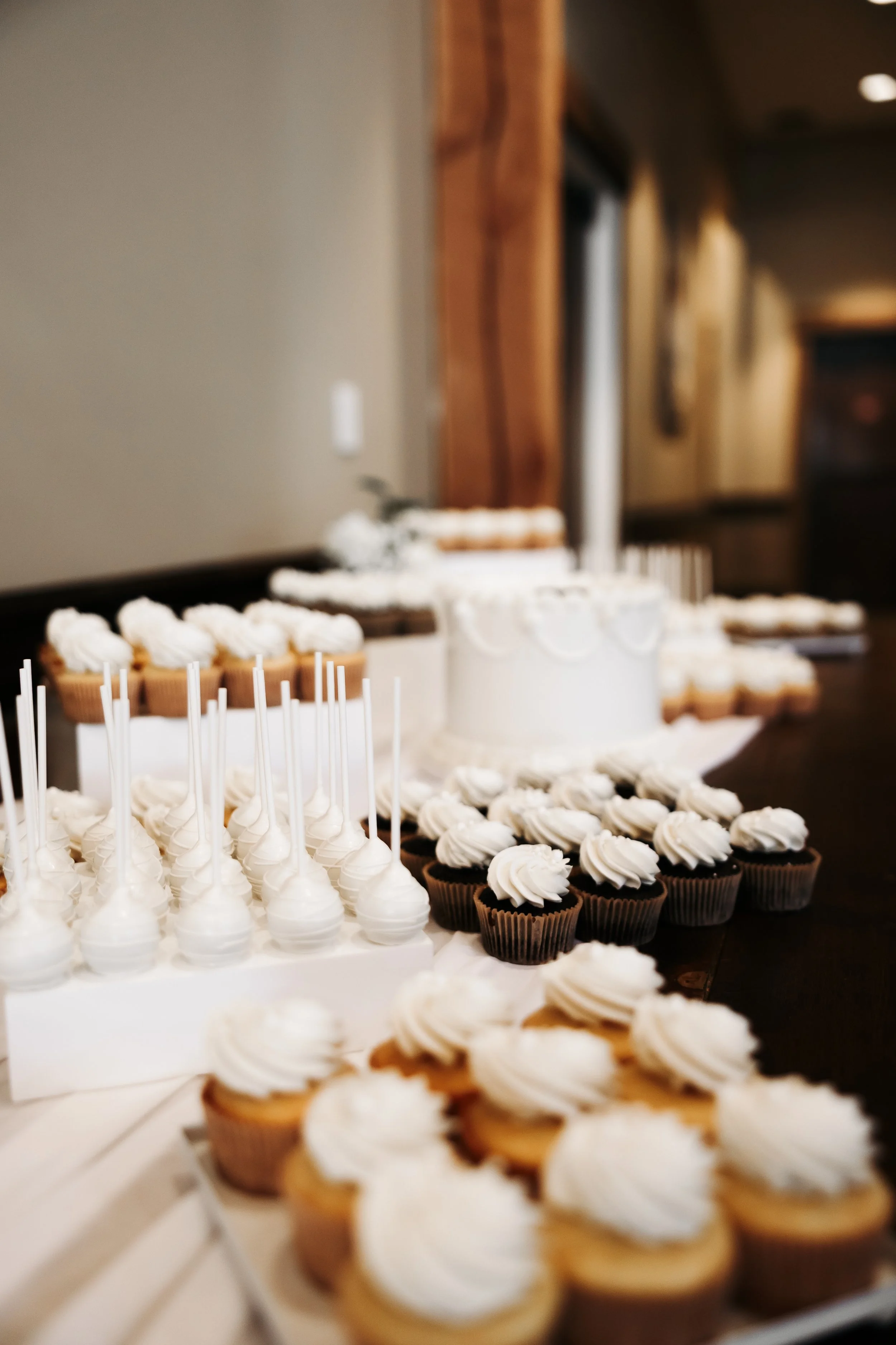 Assorted cupcakes and a white wedding cake on a table at a celebration.