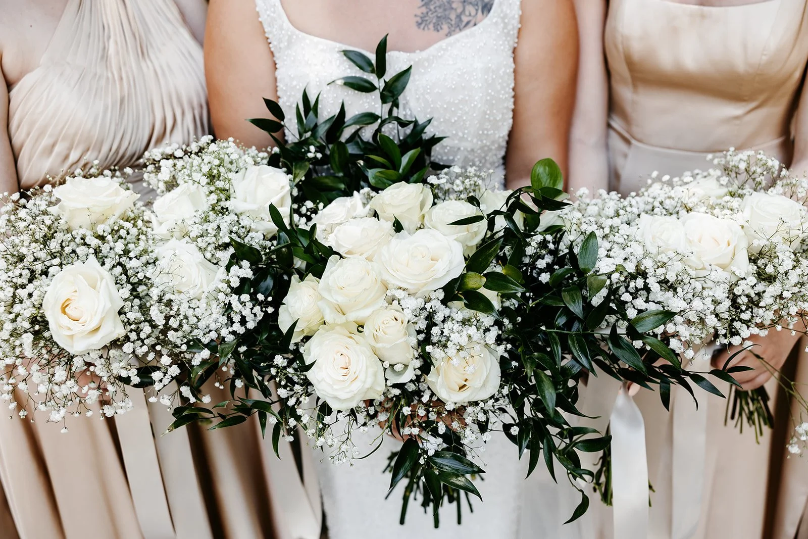 Wedding bouquet featuring white roses, baby's breath, and greenery held by a bride in a white dress.