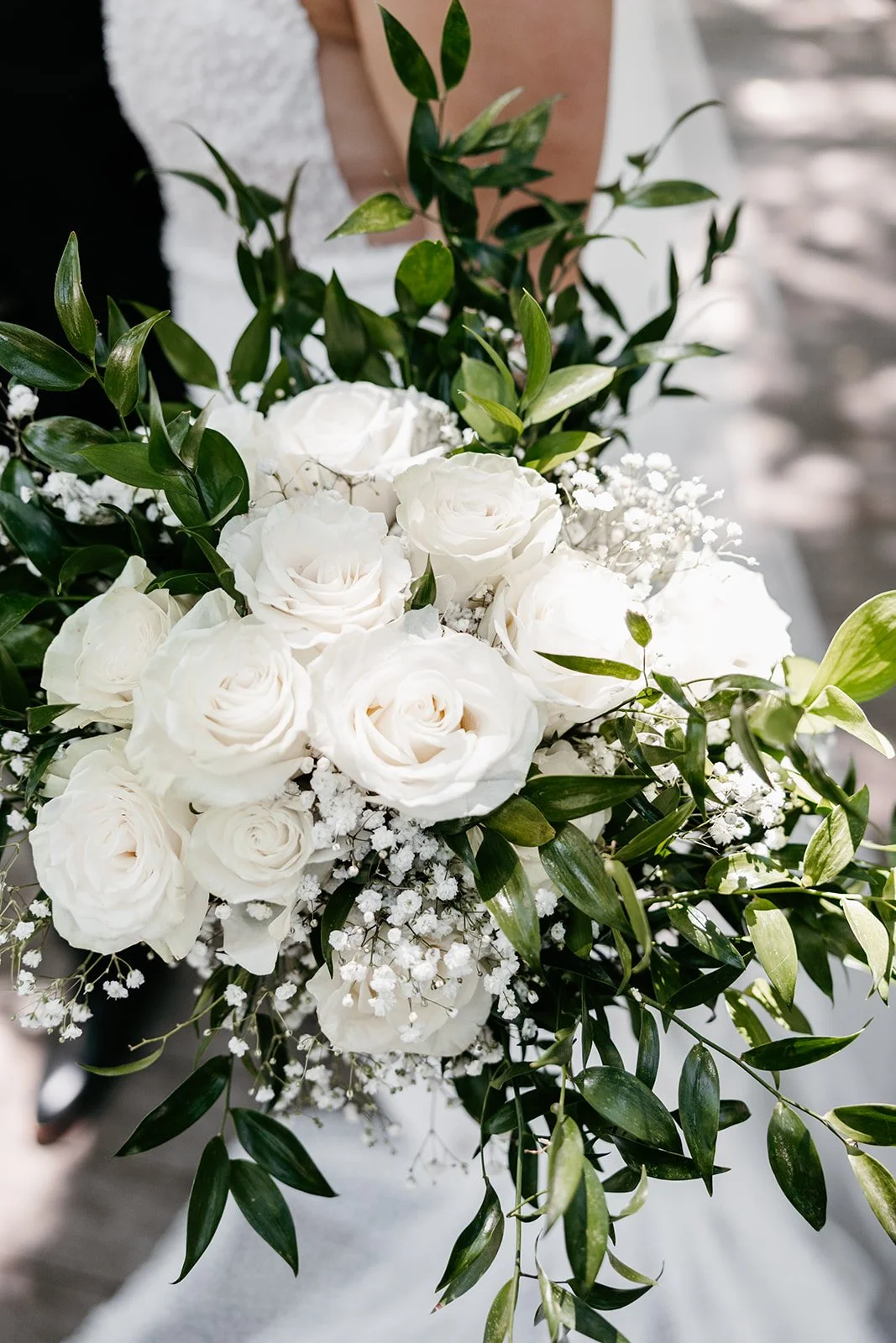 A bouquet of white roses, baby's breath, and green foliage.