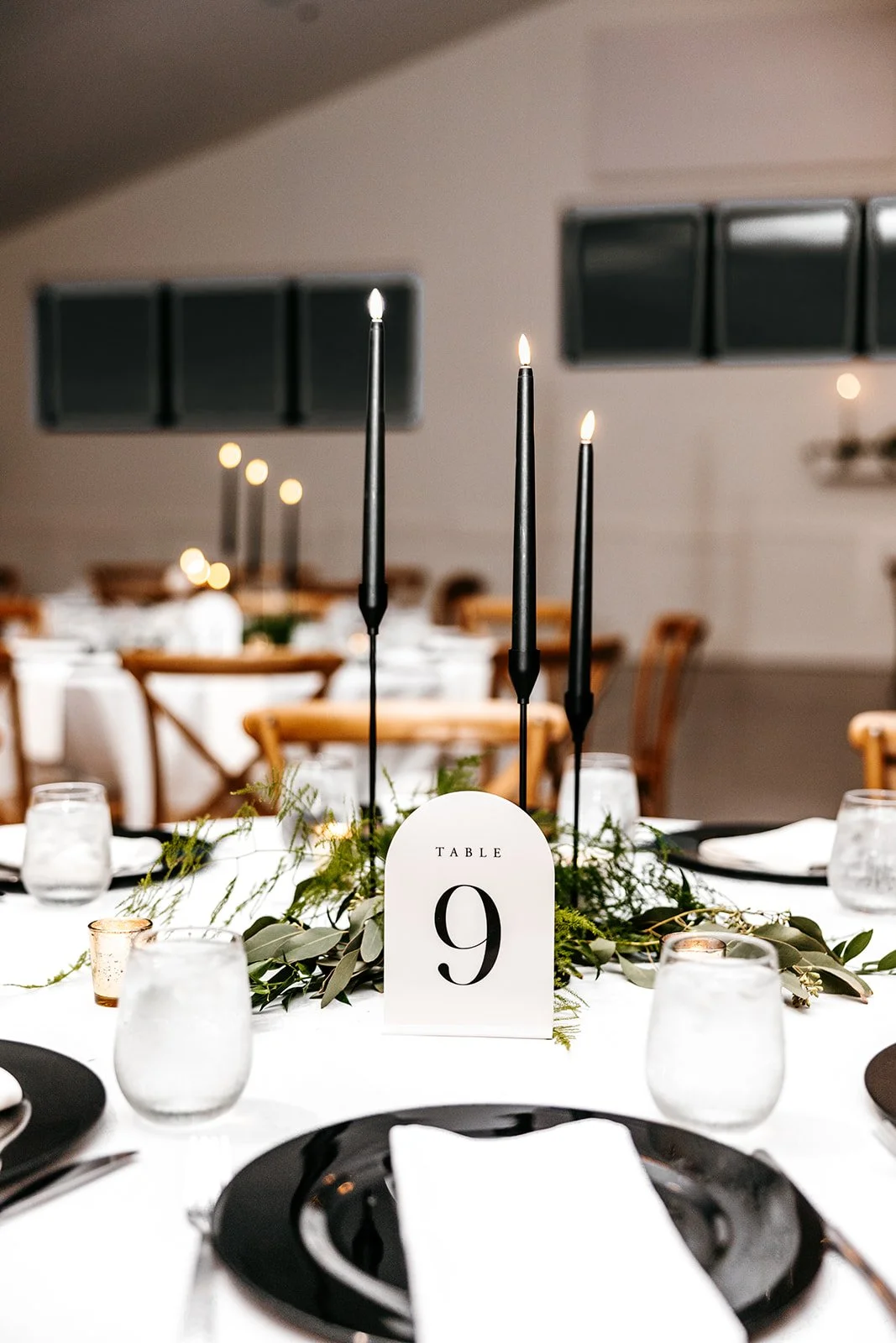Elegant wedding table decorated with black candles, greenery, and a white table number card labeled 'Table 9' in black text.