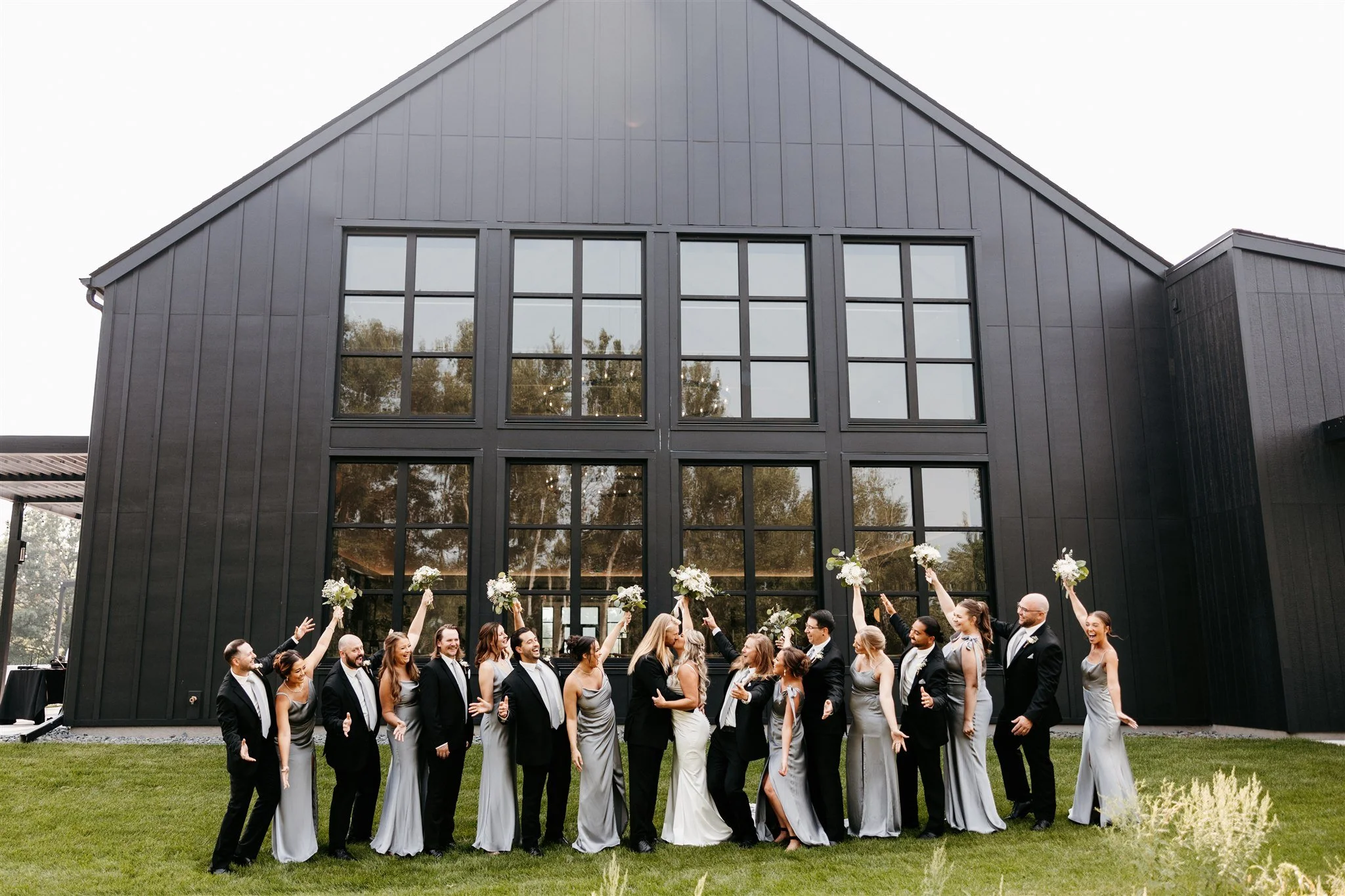 Group of wedding guests posing with bouquets in front of a modern black building with large windows