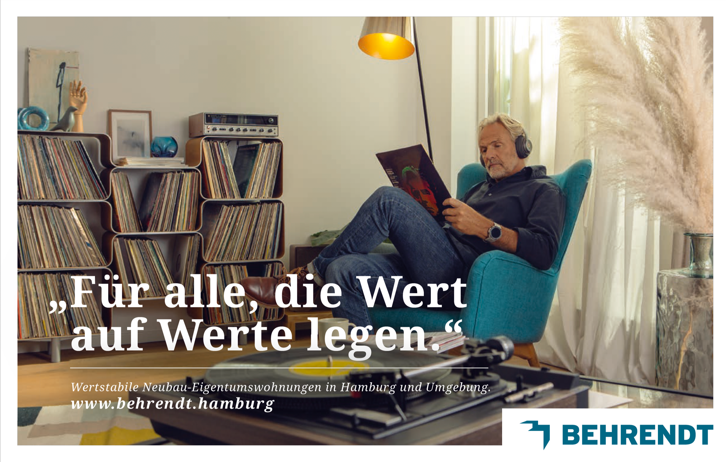 Ein älterer Mann sitzt in einem blauen Sessel, trägt Kopfhörer und liest ein Magazin. Im Hintergrund ein Fenster, eine Stehlampe Auf einem Tisch im Vordergrund befinden sich eine Turntable und ein Verpackung. Links im Bild eine Bücherregal mit vielen