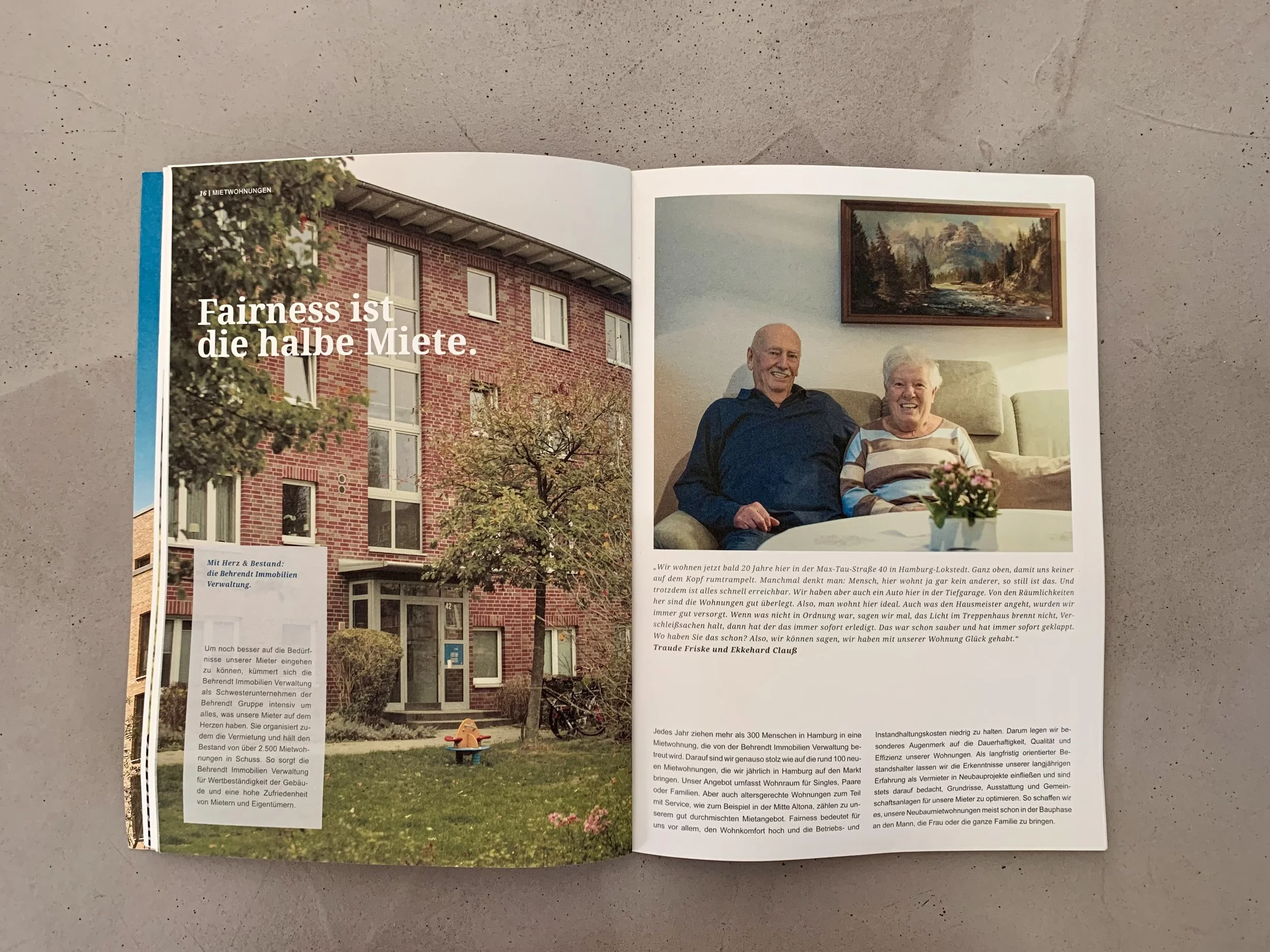 Offene Zeitschrift mit einem Bild eines Mehrfamilienhauses im Außenbereich und einem Bild eines älteren Paares, das auf einem Sofa im Wohnzimmer sitzt, mit einem Gemälde an der Wand.