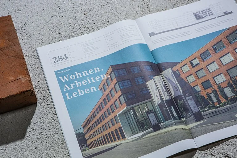 Offener Magazin oder Broschüre mit einem Bild eines modernen mehrstöckigen Gebäudes auf der Seite, mit dem Titel "Wohnen. Arbeiten. Leben." in deutscher Sprache.