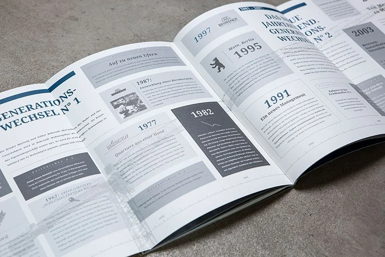 Broschüre mit einer Zeitleiste der Generationen, die Jahre 1952 bis 2003 abdeckt, mit Texten und Grafiken, auf einem grauen Tisch.