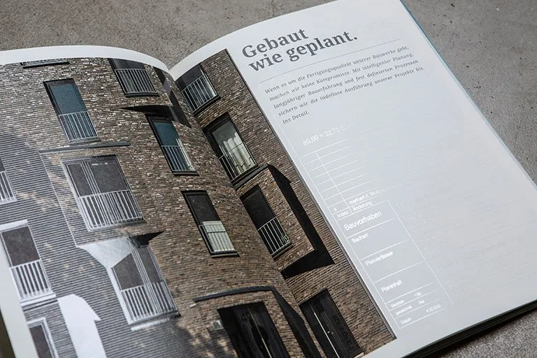 Offener Bau- und Planungskatalog mit Bild eines modernen, braunen Mehrparteienhauses und Text in Deutsch.