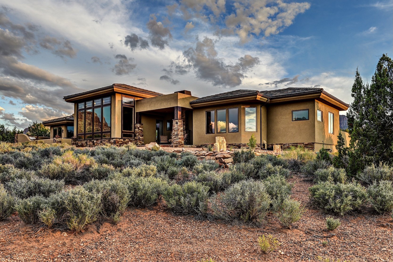Modern house with large windows in a desert landscape during sunset.