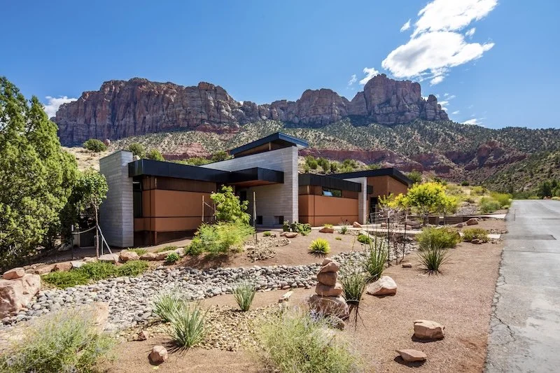 Modern house with desert landscaping and mountains in the background under a partly cloudy sky.