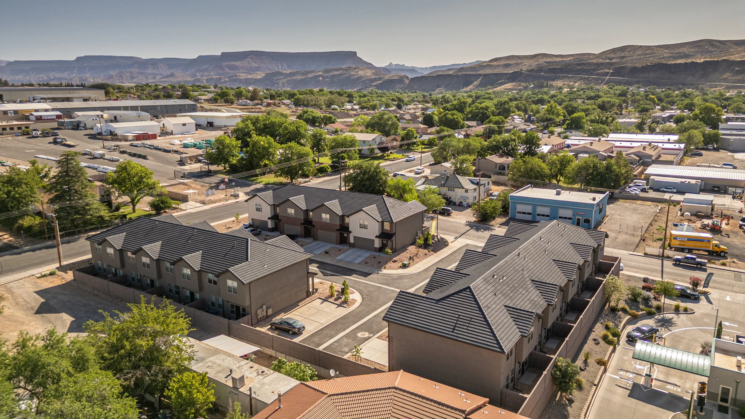 Aerial view of a residential area with apartment buildings, parking lots, and trees, set against a backdrop of mountains and a distant town.