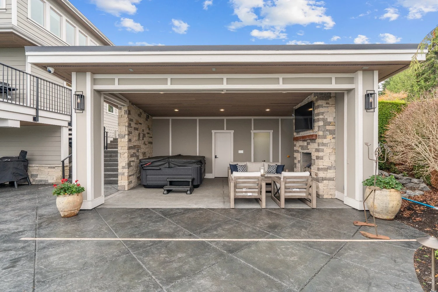 Outdoor patio area with seating, a hot tub, a wall-mounted TV, and brick accents.