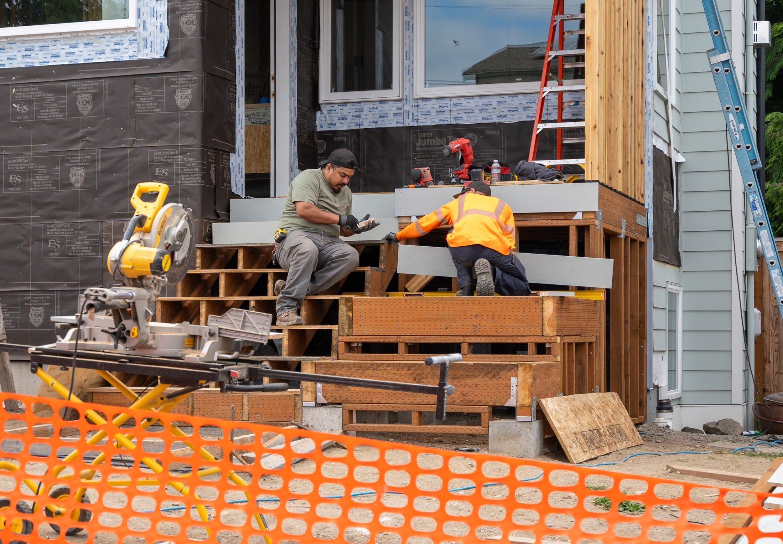 Construction workers building the front porch of a house, with tools and materials around them.