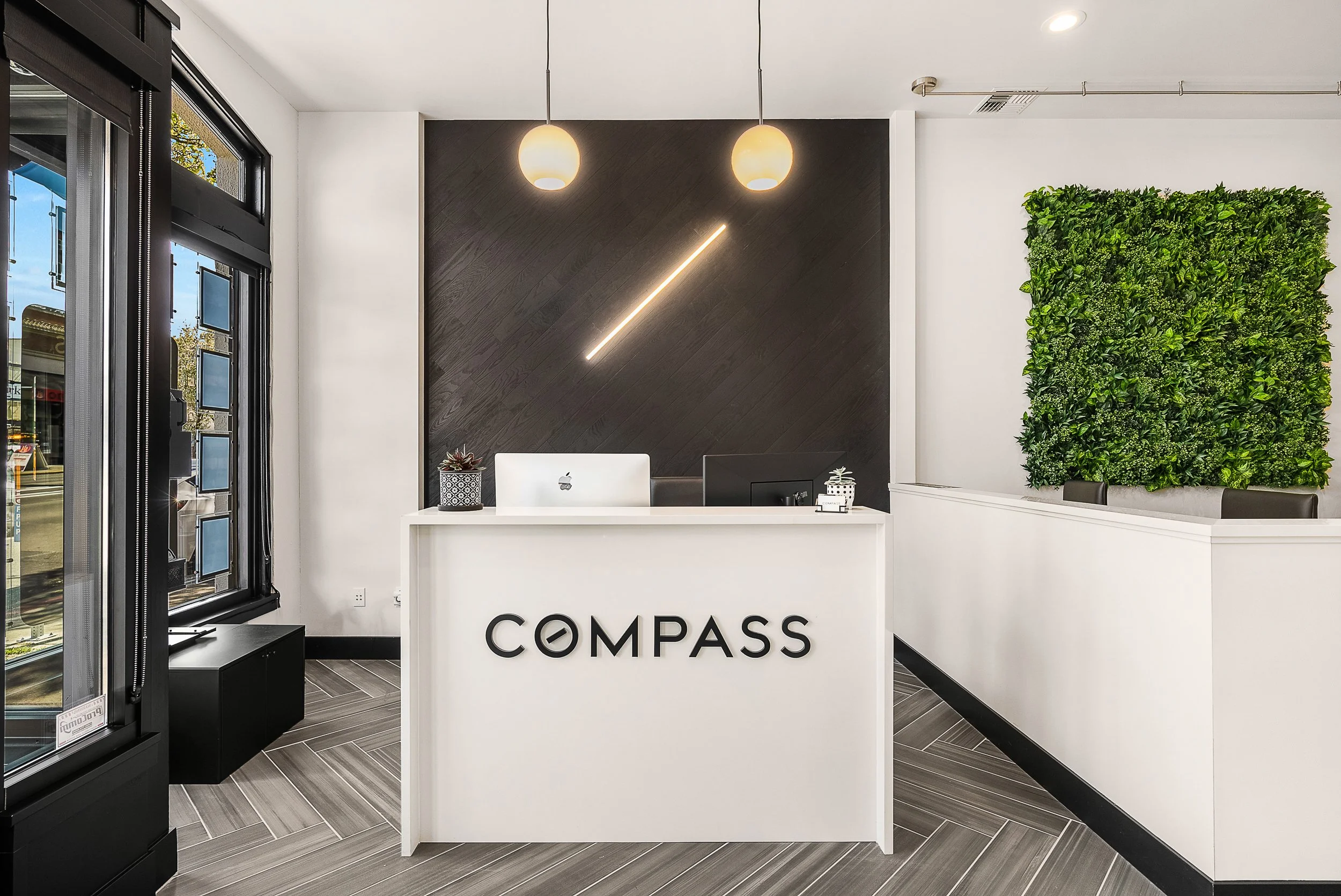 Reception desk with the sign 'COMPASS' in a modern office lobby featuring a green wall and black and white decor.