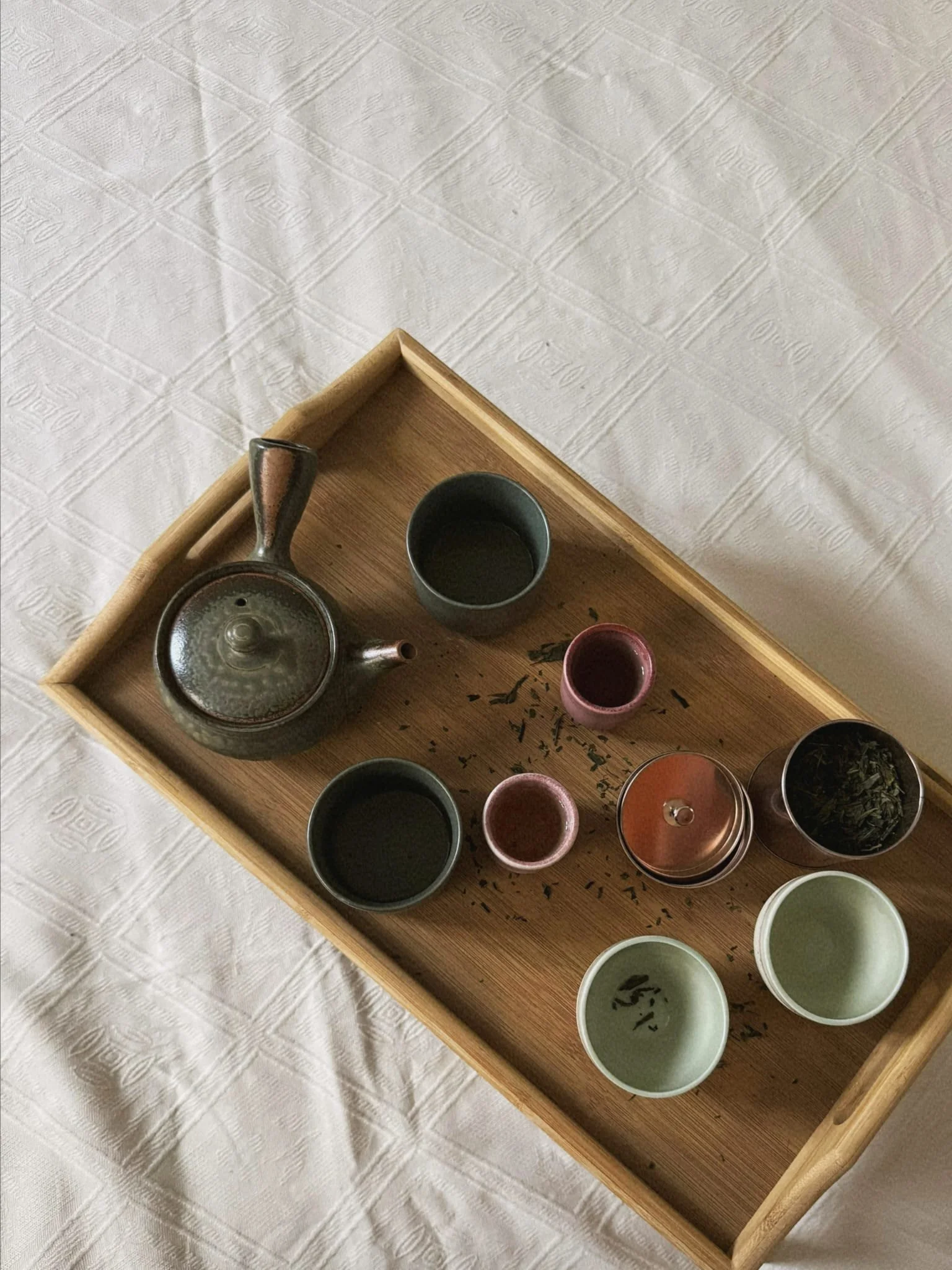Ein Holztablett mit Teekanne, Teeschalen und lose Teeblätter auf einem weißen Tischtuch.