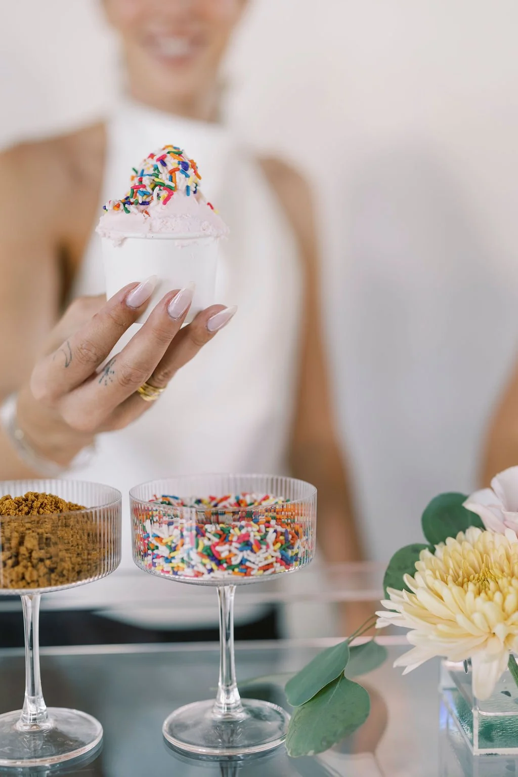 A woman holding a glass of pink ice cream with rainbow sprinkles.