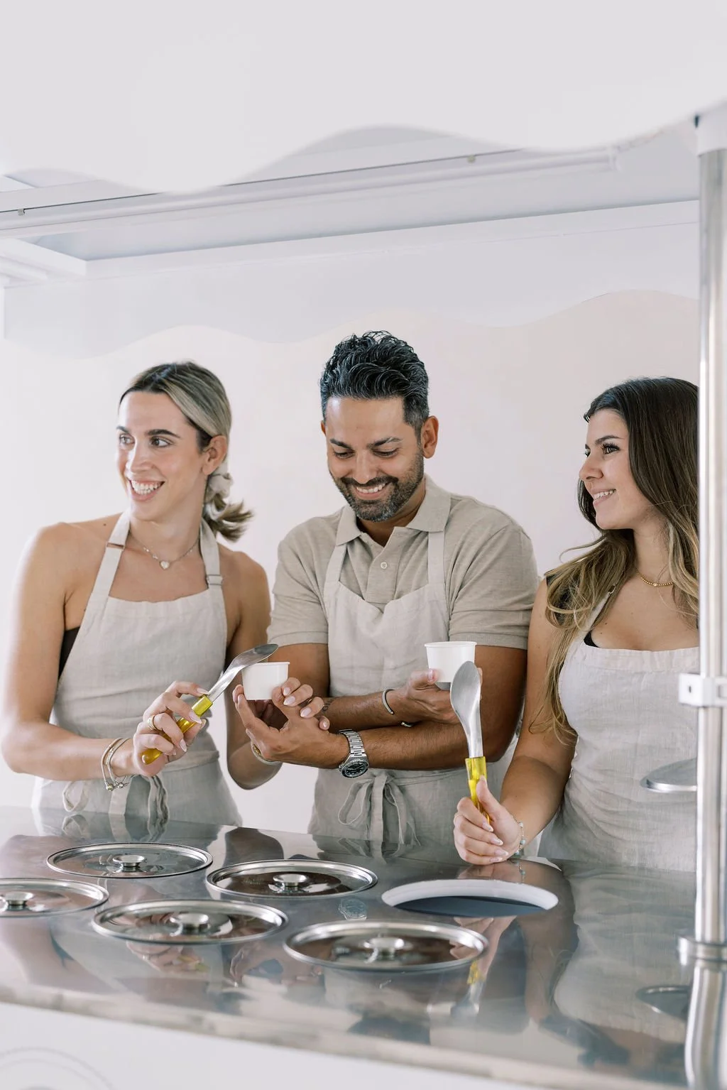 Three people, two women and one man, smiling and serving ice cream at an ice cream shop counter.
