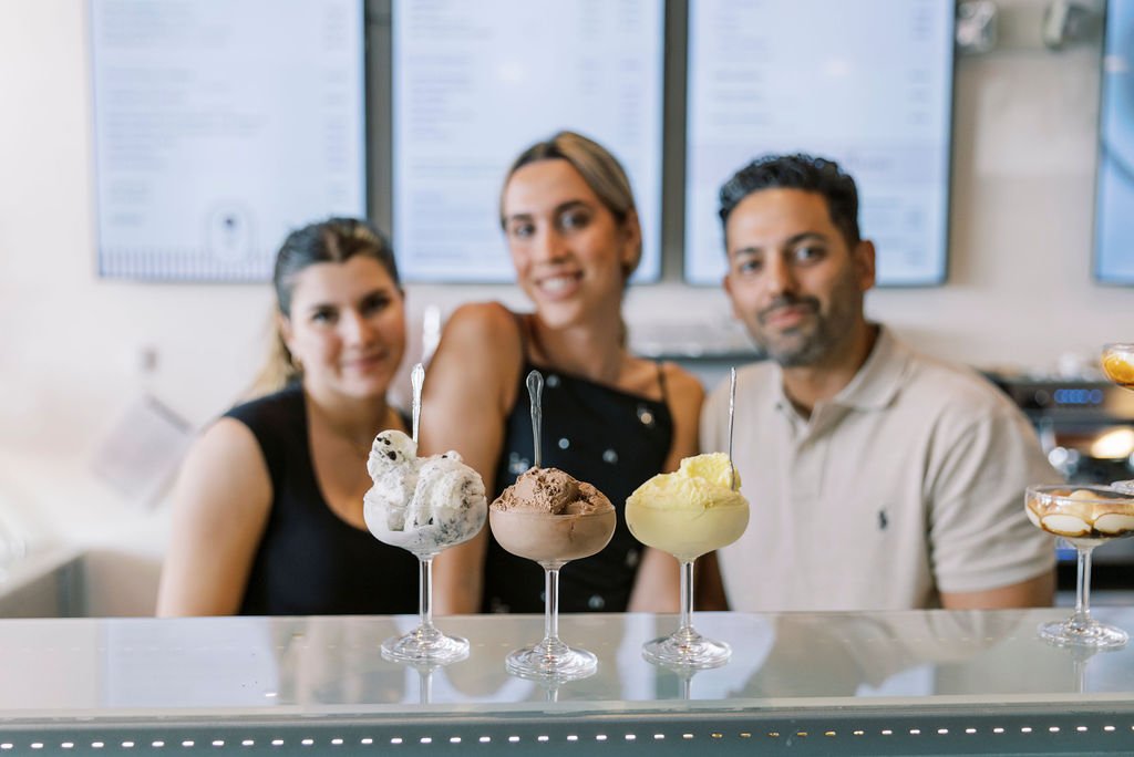 Three people behind a counter with three glasses of ice cream flavors in front of them