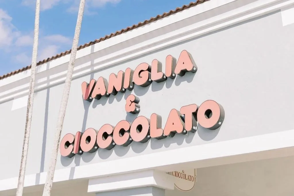 Sign on a building reading "Vaniglia & Cioccolato" with white walls and a tiled roof, under a blue sky.