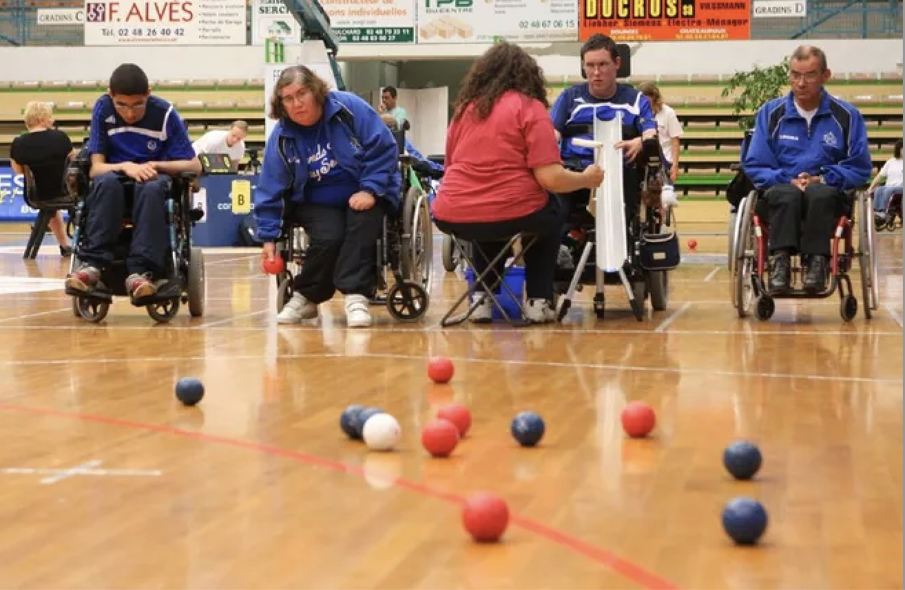 Des personnes en fauteuil roulant jouent à la boccia dans un gymnase.