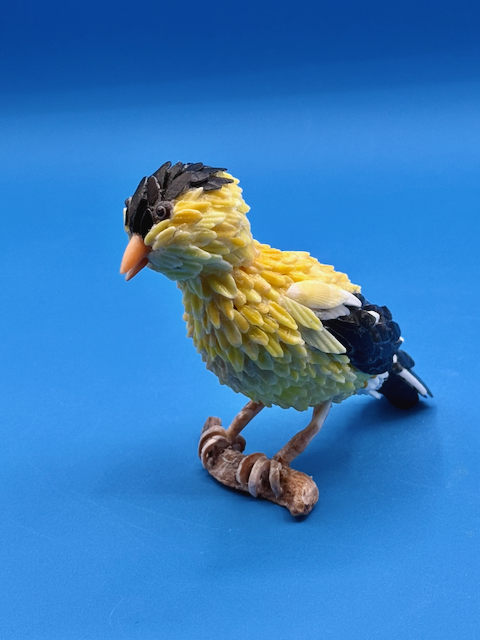Handcrafted goldfinch shell sculpture perched on driftwood coastal wildlife art.
