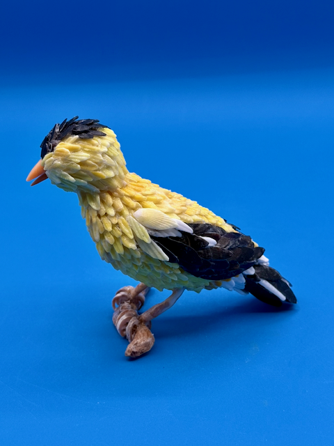 Handcrafted goldfinch shell sculpture perched on driftwood coastal wildlife art.