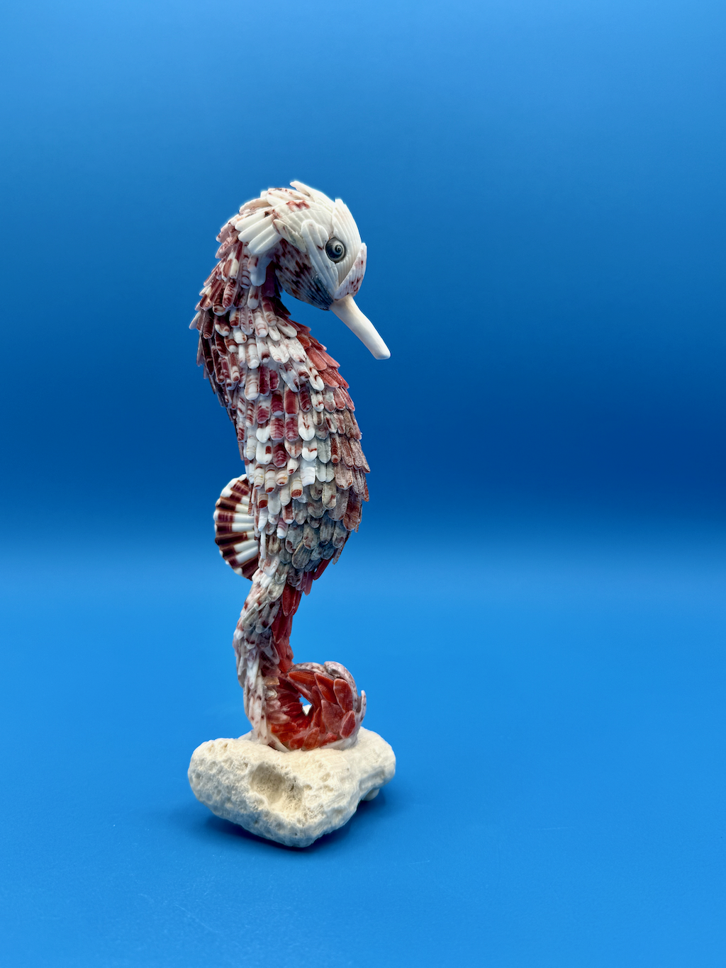 Spiral handcrafted seahorse sculpture made from calico scallop, whelk, and moon snail shells, mounted on a vintage coral base, standing 7.5 inches tall.