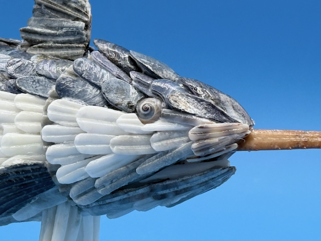 Close up view of a handcrafted marlin sculpture made from natural seashells with a textured blue-gray back, silvery-white underside, sculpted fins, and long bill.