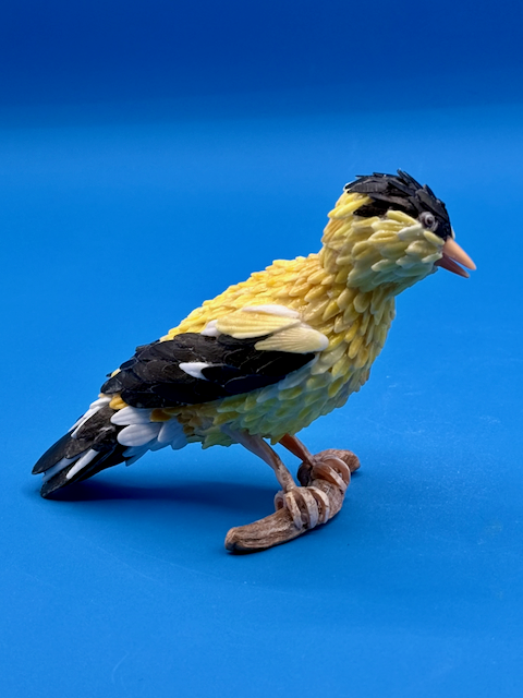 Handcrafted goldfinch shell sculpture perched on driftwood coastal wildlife art.