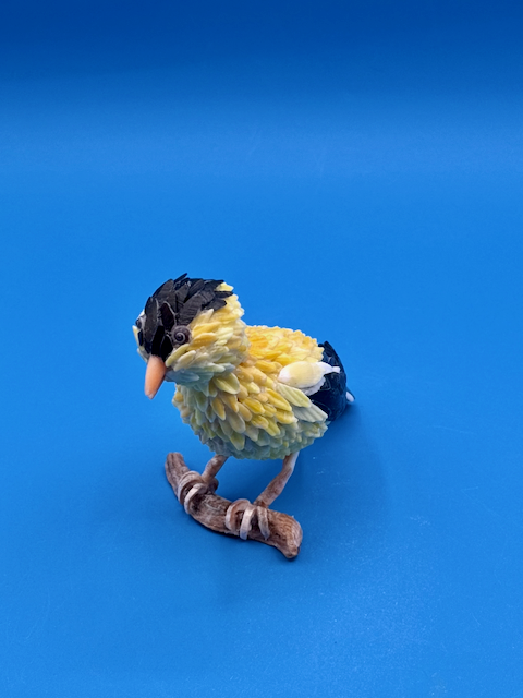 Handcrafted goldfinch shell sculpture perched on driftwood coastal wildlife art.