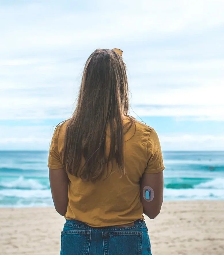 T1D adult as she stares at the ocean, wearing a Dexcom on her arm. This represents healing from diabetes burnout after diabetes therapy in Orange County, California, North Carolina, or PSYPACT States
