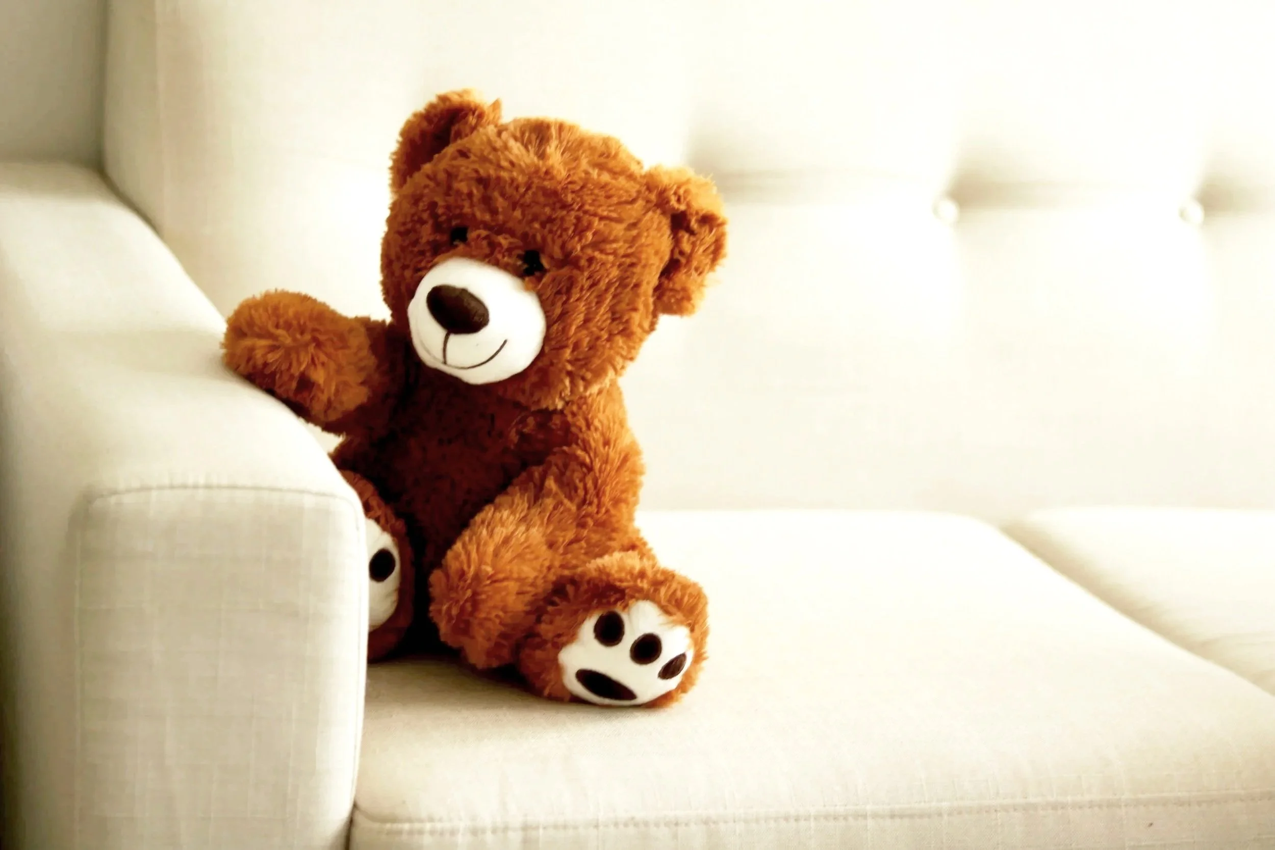 Teddy Bear sitting on cream colored couch. This is a PCIT therapy prop named Mr. Bear, to help with child behavior problems in Orange County, California, North Carolina, & PSYPACT States