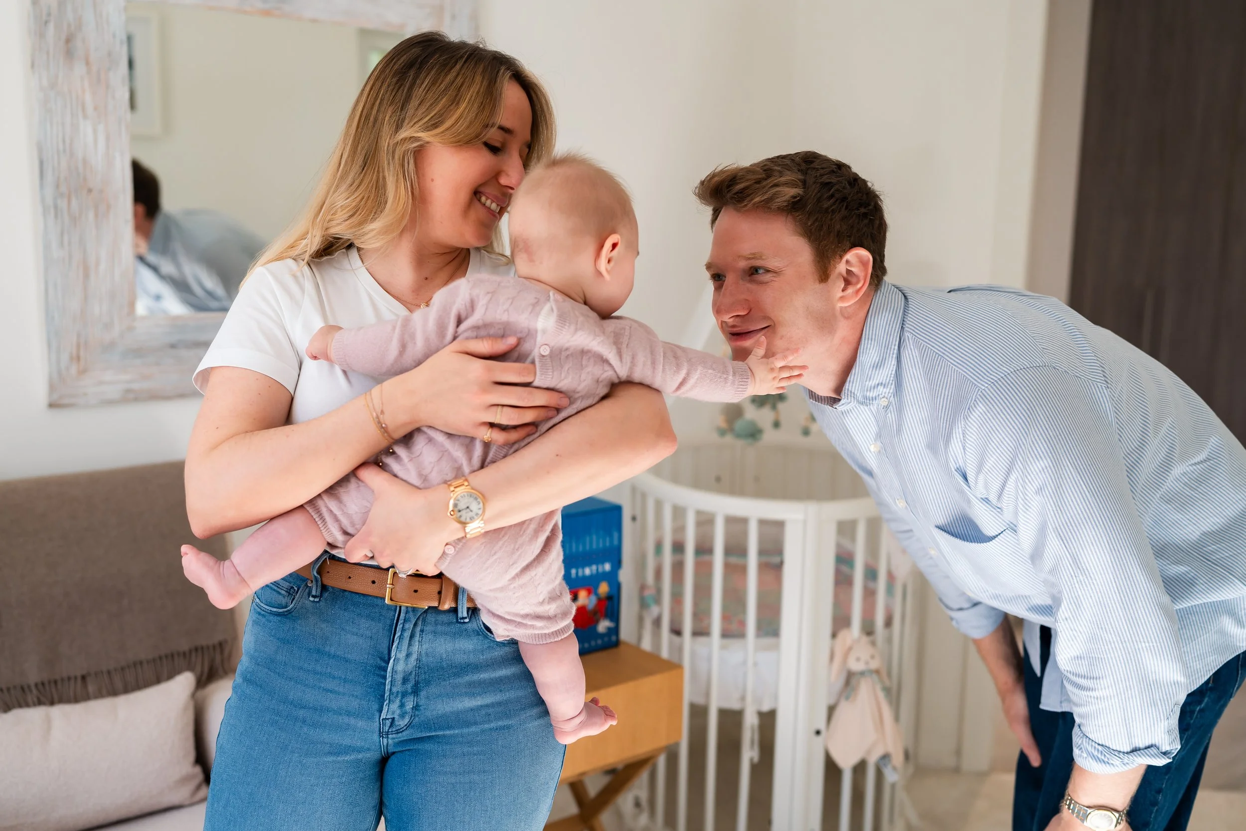 Mother holding her baby girl on her chest, smiling at the father leaning in close during an in-home family photoshoot in Geneva, Switzerland