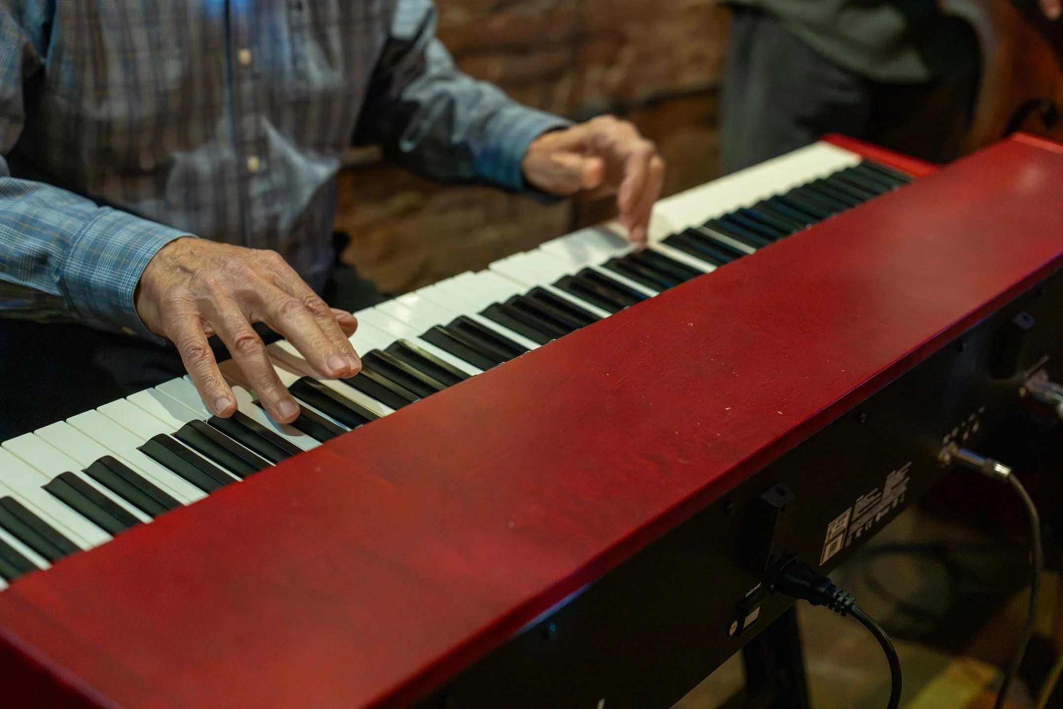 Close-up of a man’s hands playing a red digital piano keyboard indoors during a live music performance.