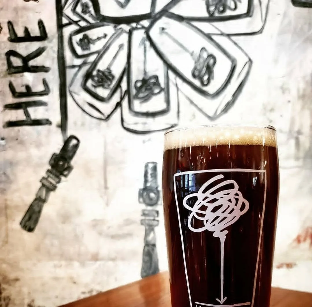 Here & Now Brewing Company's house stout is pictured in front of an artistic mural of a tap system in our brewery in honesdale, pa.