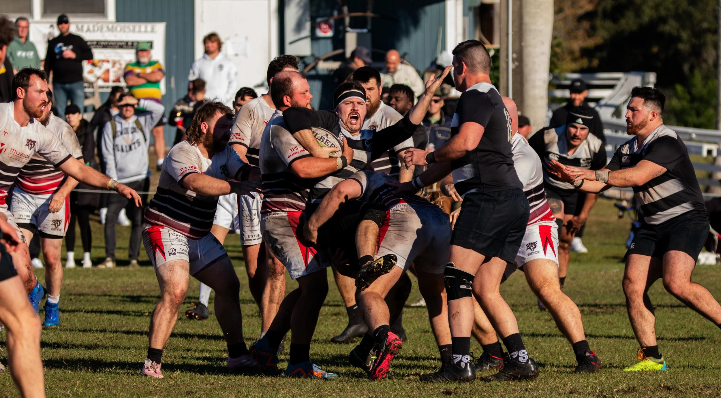 Rugby players in action during a match, with some players tackling and others trying to gain control of the ball.