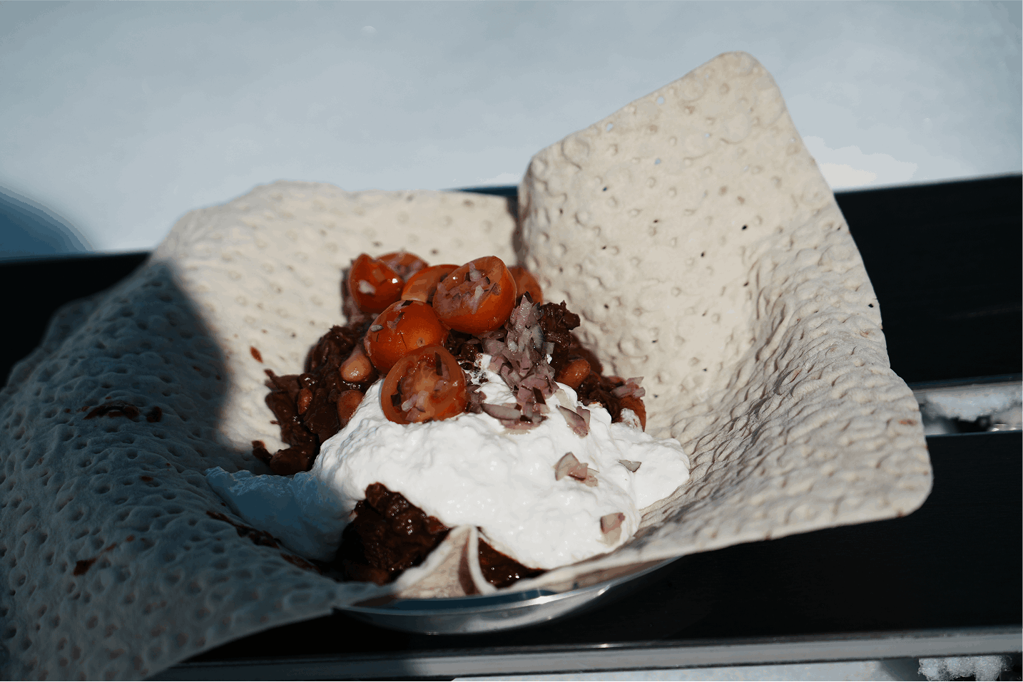 Tacos med kött, gräddfil, tomater och lök på ett serveringsfat med papper under.