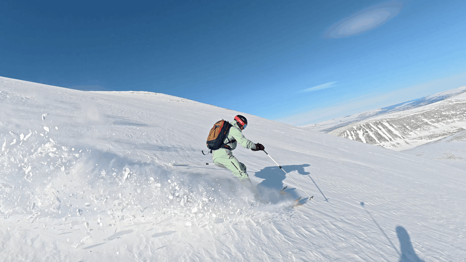 En person åker skidor nerför en snöklädd backe under en klar blå himmel.