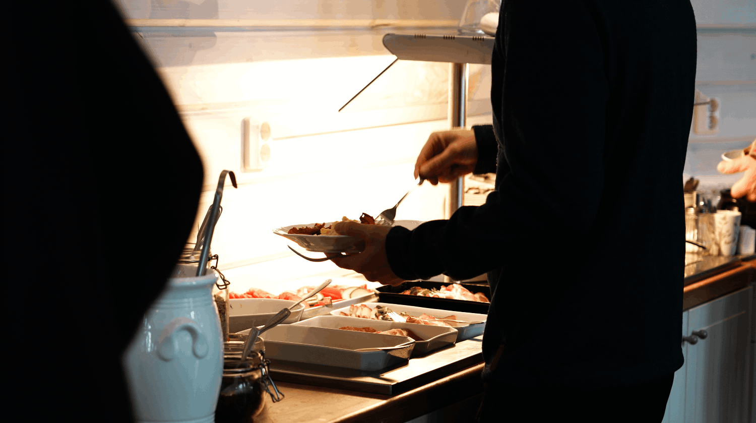 Person som serverar mat vid en buffé i ett kök eller restaurangmiljö.