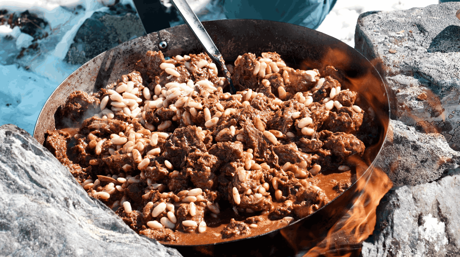 Stekt kött med pinjenötter i en panna över öppen eld utomhus.