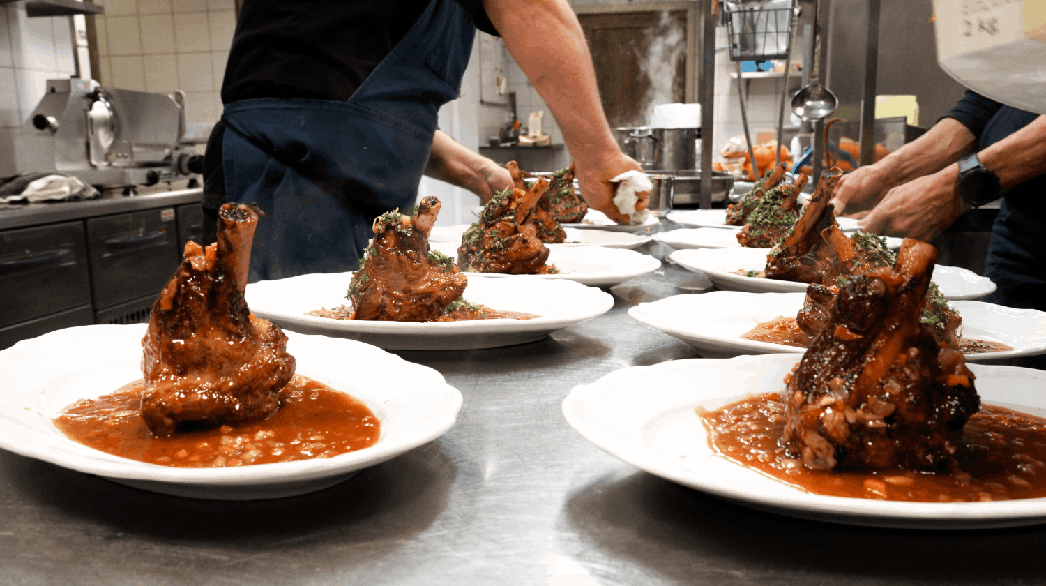 Kockar förbereder och serverar kötträtter med sås på en köksbänk.