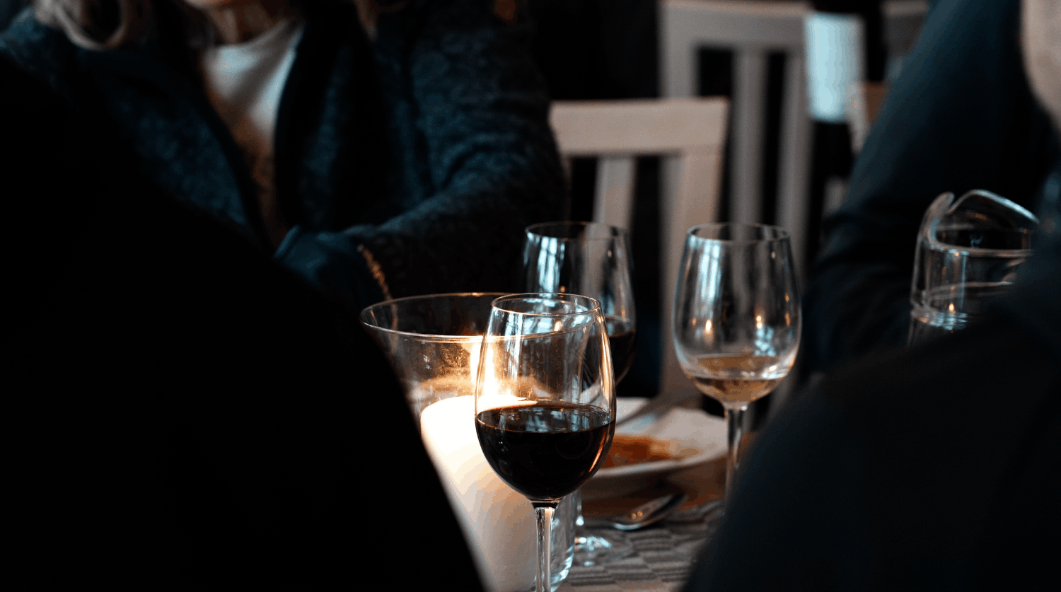 Glass med rödvin på ett bord omgiven av personer.
