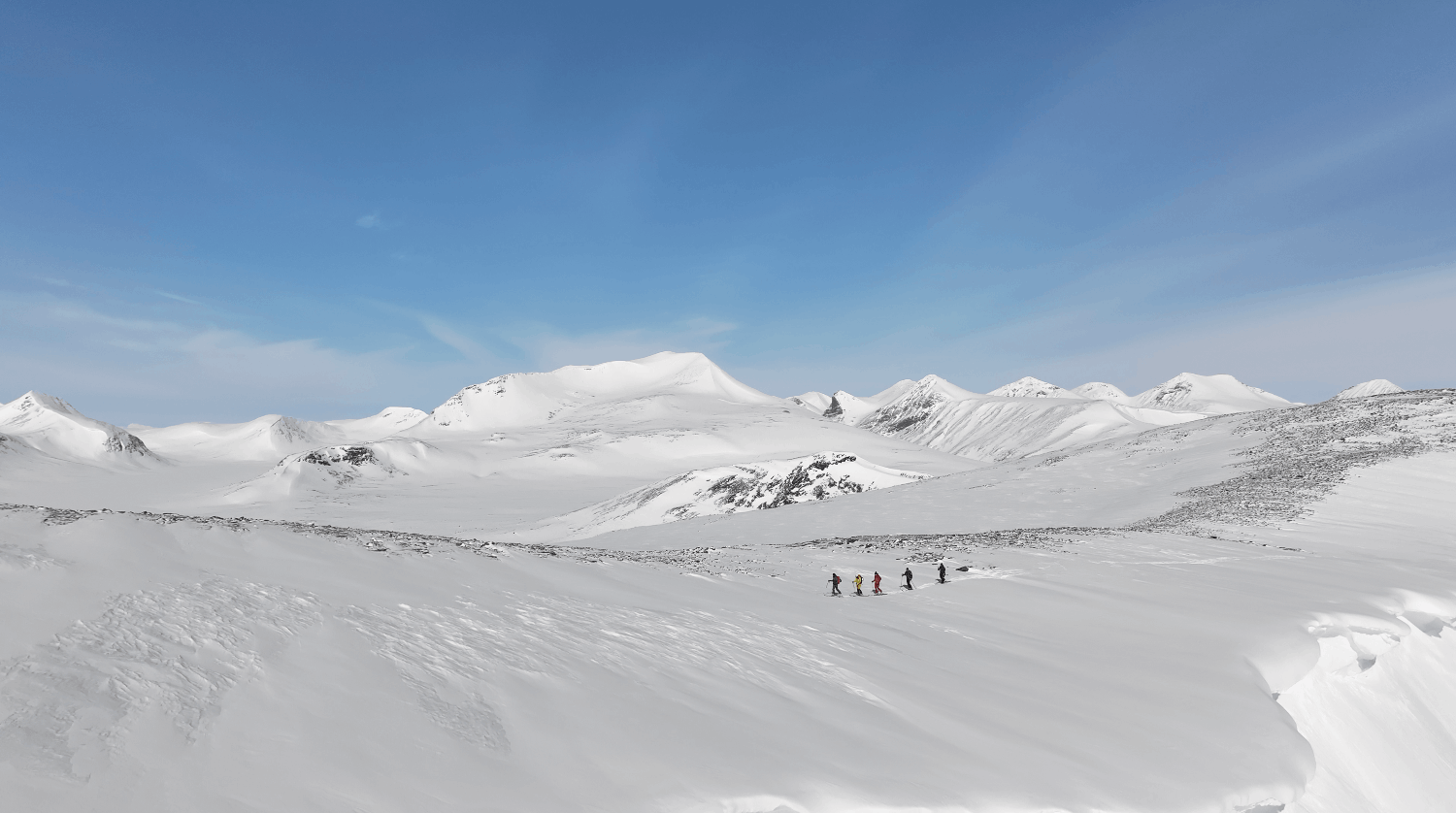 Skidåkare i snötäckta fjälllandskap under blå himmel.