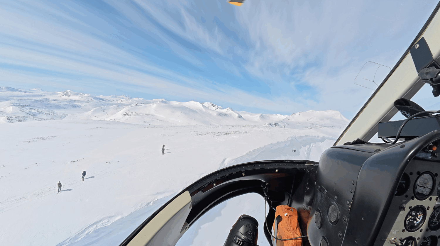 Utsikt från helikopterfönster över snötäckta berg och landskap med tre personer som gick i snön.