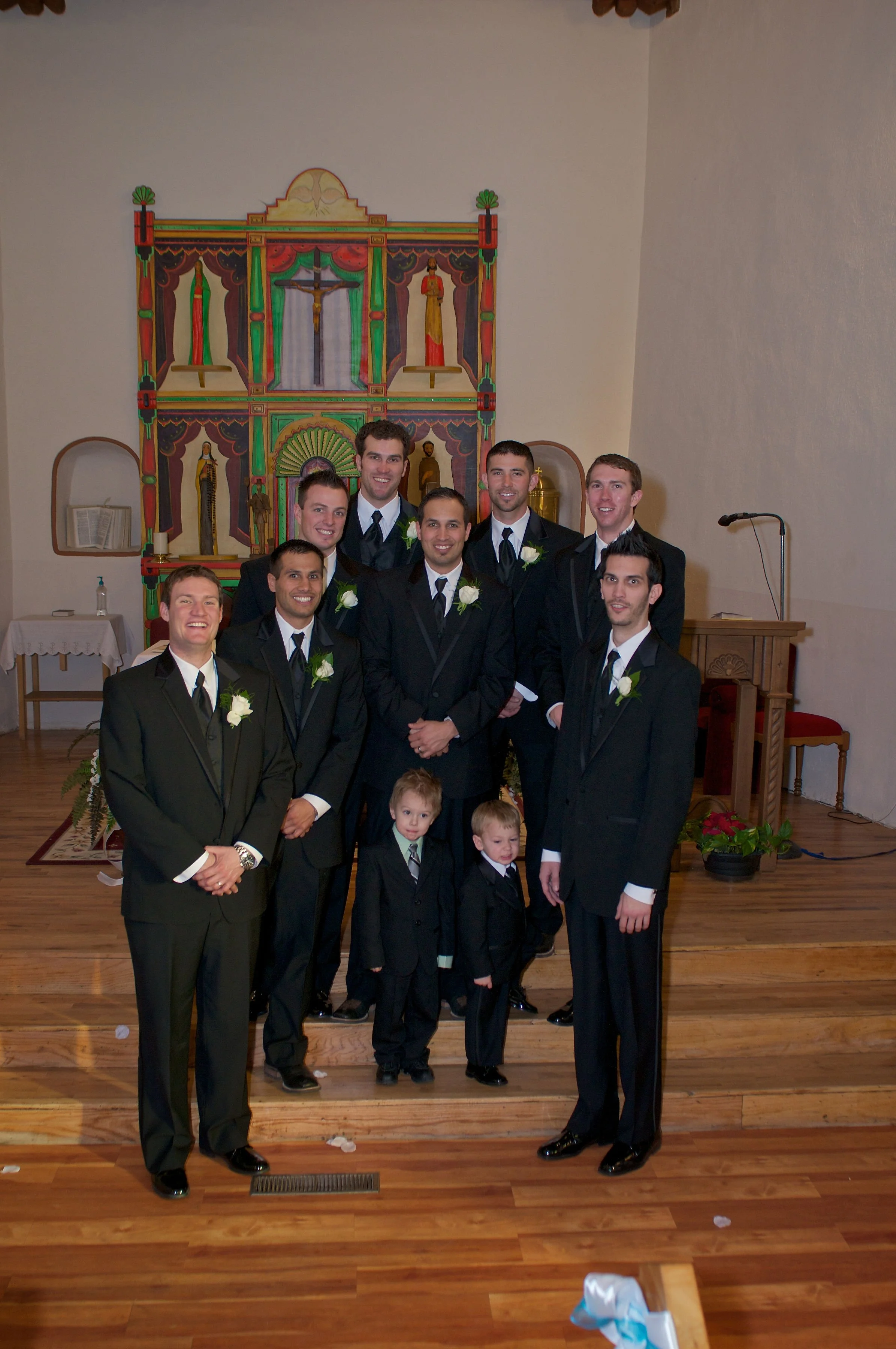 A group of men and two young boys dressed in formal suits standing inside a church, smiling for a photo.
