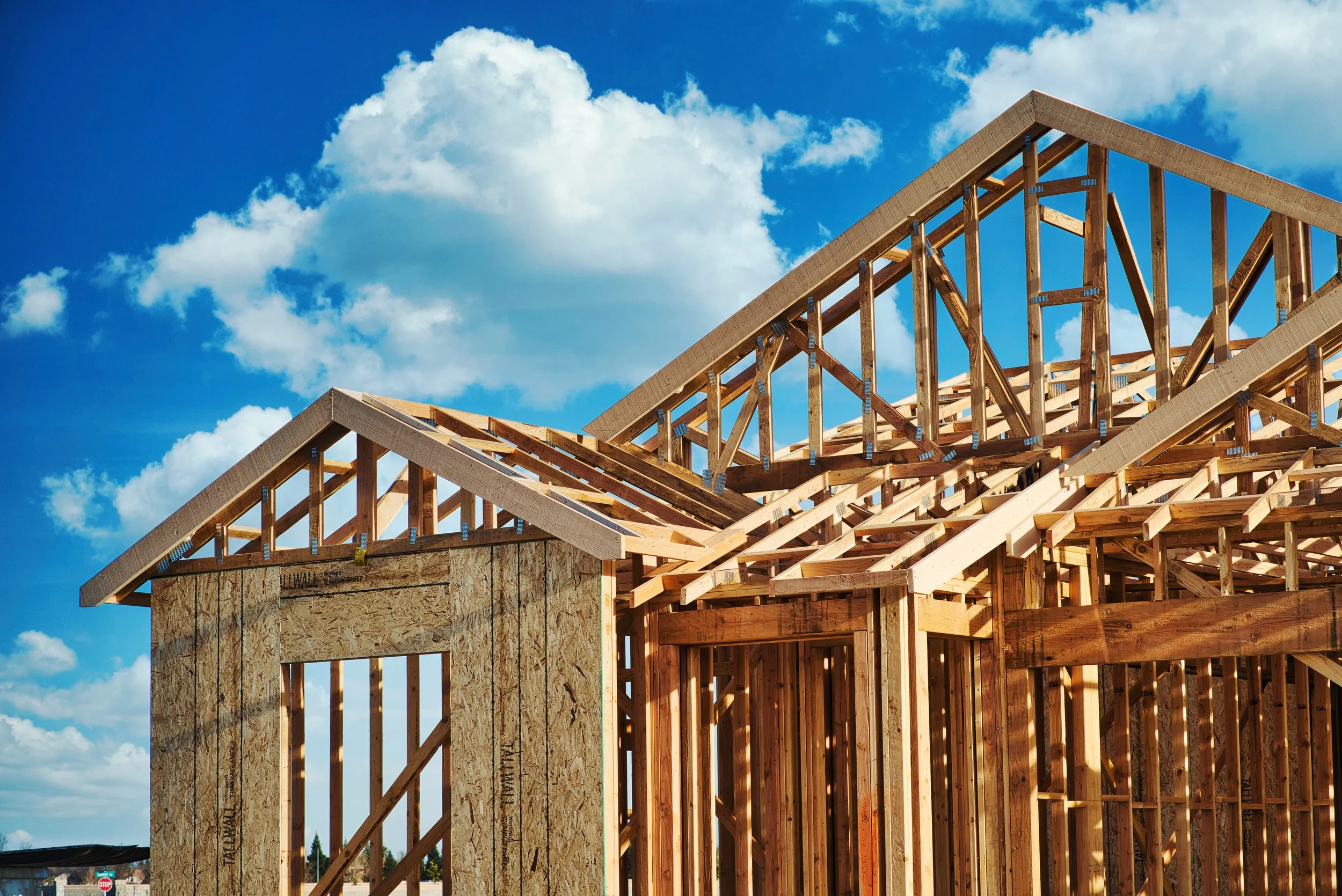 Wood framing for a house under construction against a blue sky with clouds.