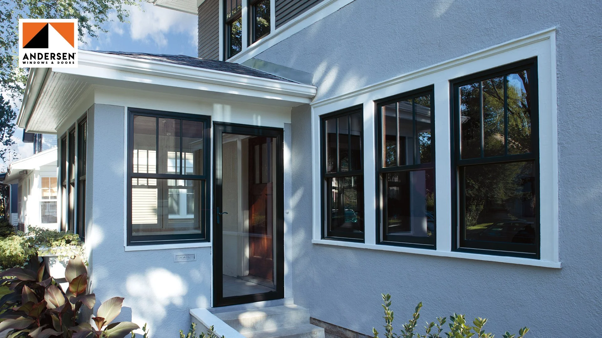 Exterior view of a house showing multiple windows and a glass door, with a sign for Andersen Windows & Doors in the top left corner.