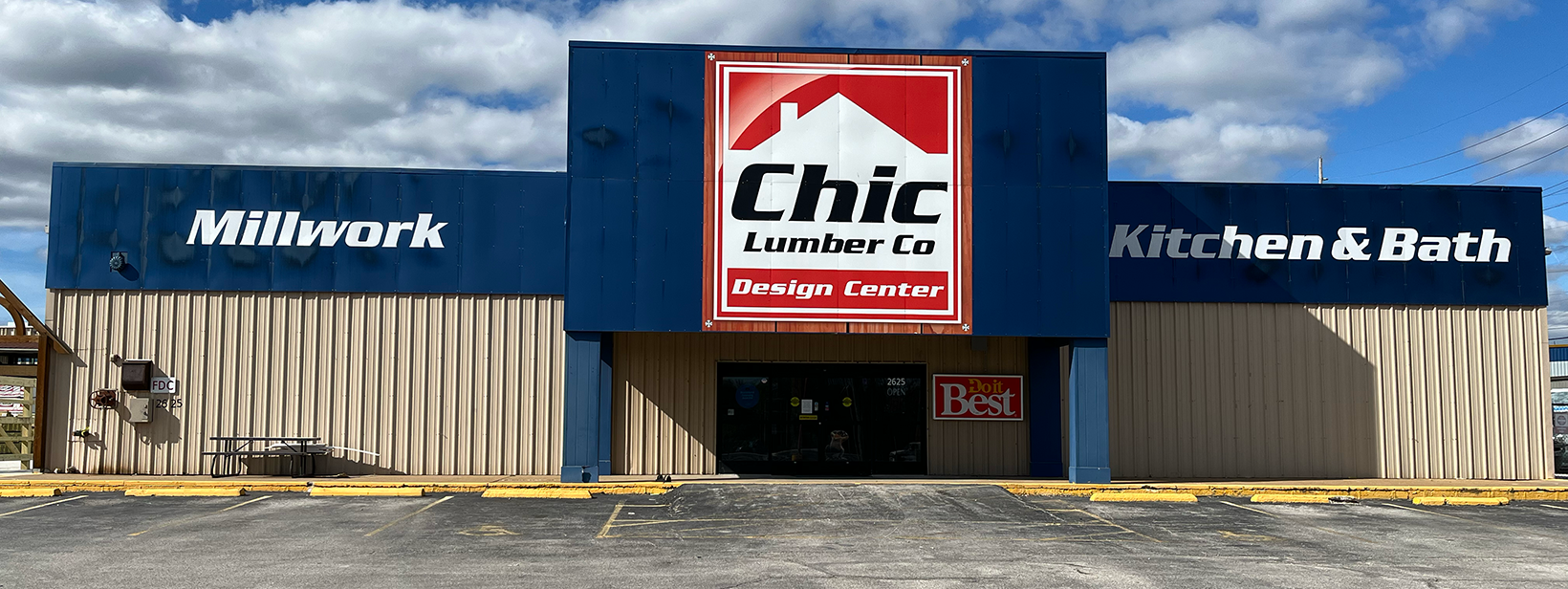 Exterior view of Chic Lumber Co Design Center, a building with beige and blue siding, large signage for Milwork and Kitchen & Bath, a parking lot in front, and a partly cloudy sky.