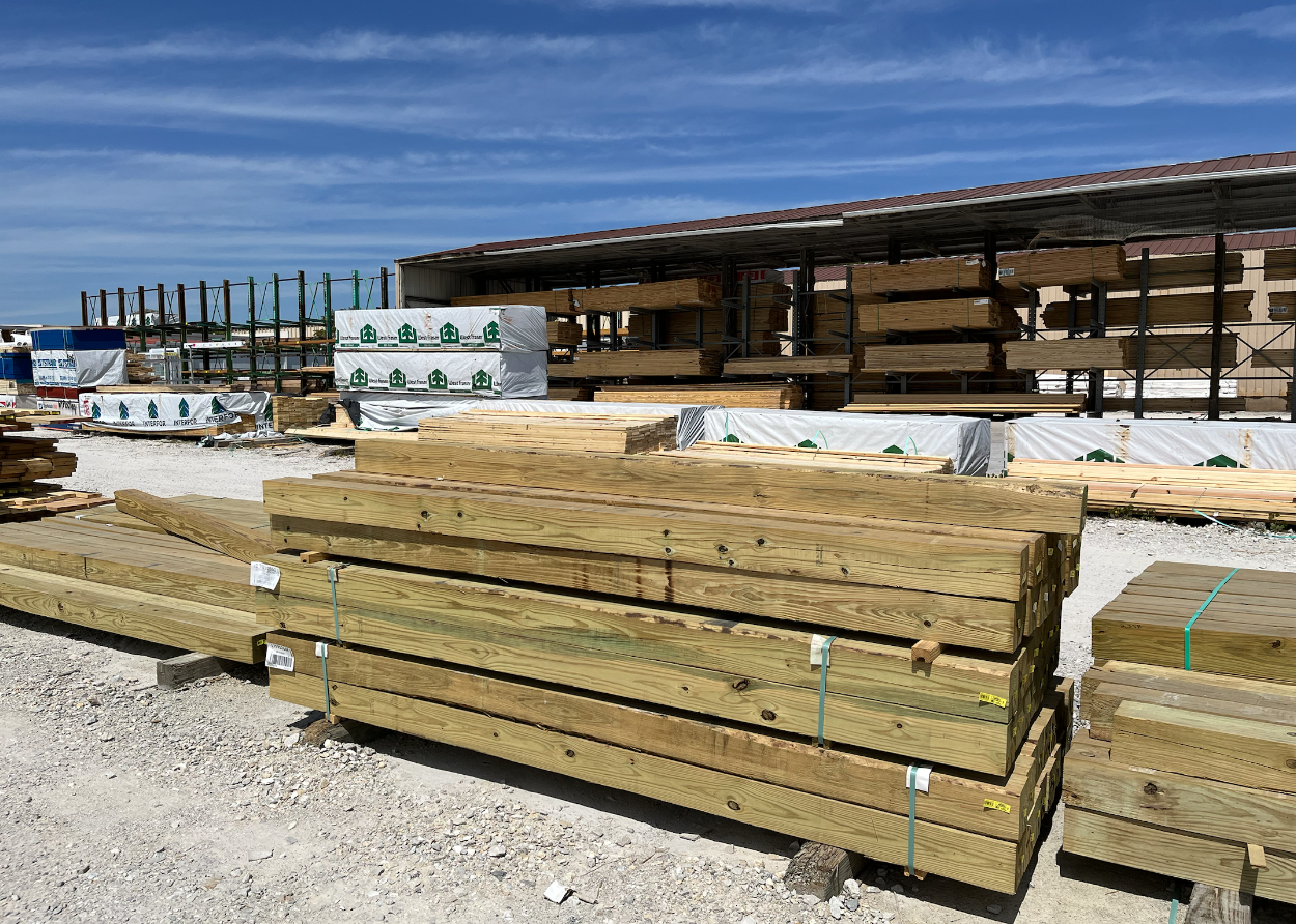 Stacks of lumber and construction materials at a hardware store or construction site with a blue sky overhead.