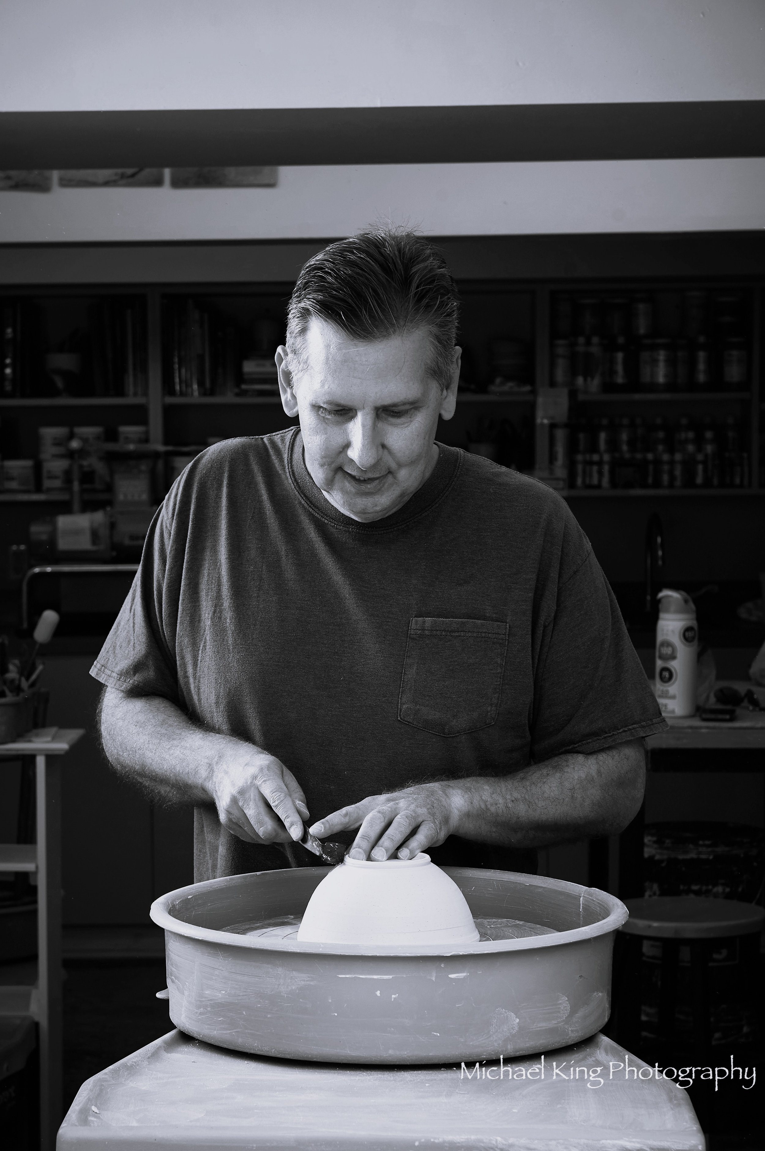 A man working on pottery, shaping a ceramic piece on a potter's wheel in a studio.