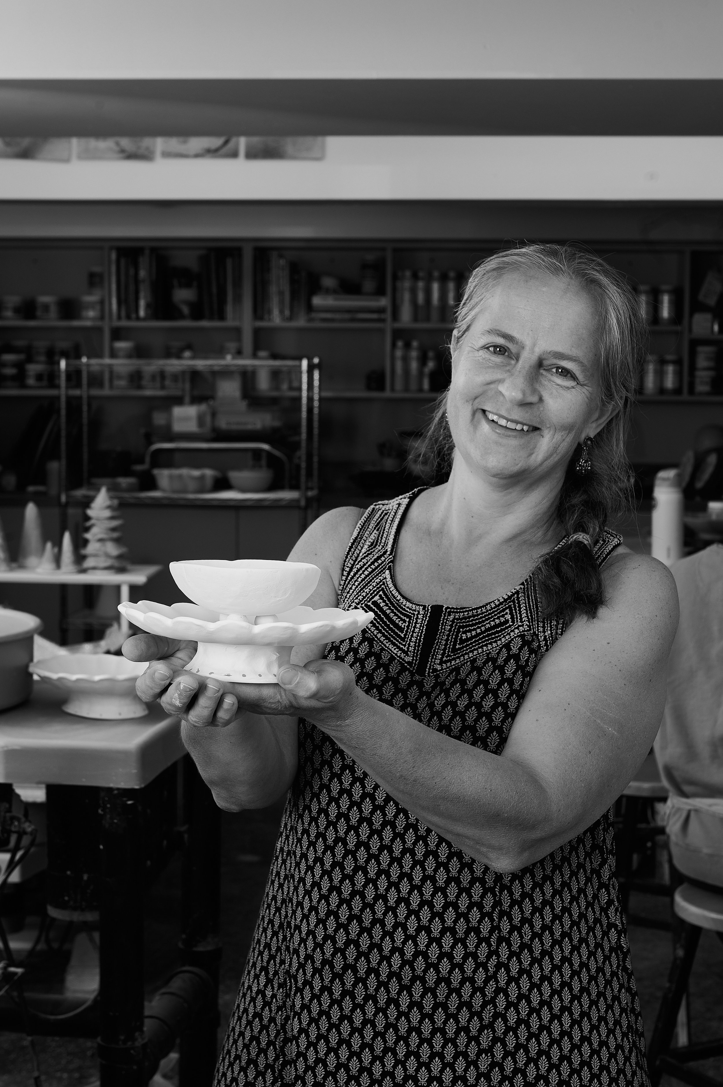 A woman smiling and holding a ceramic sculpture in a pottery studio.