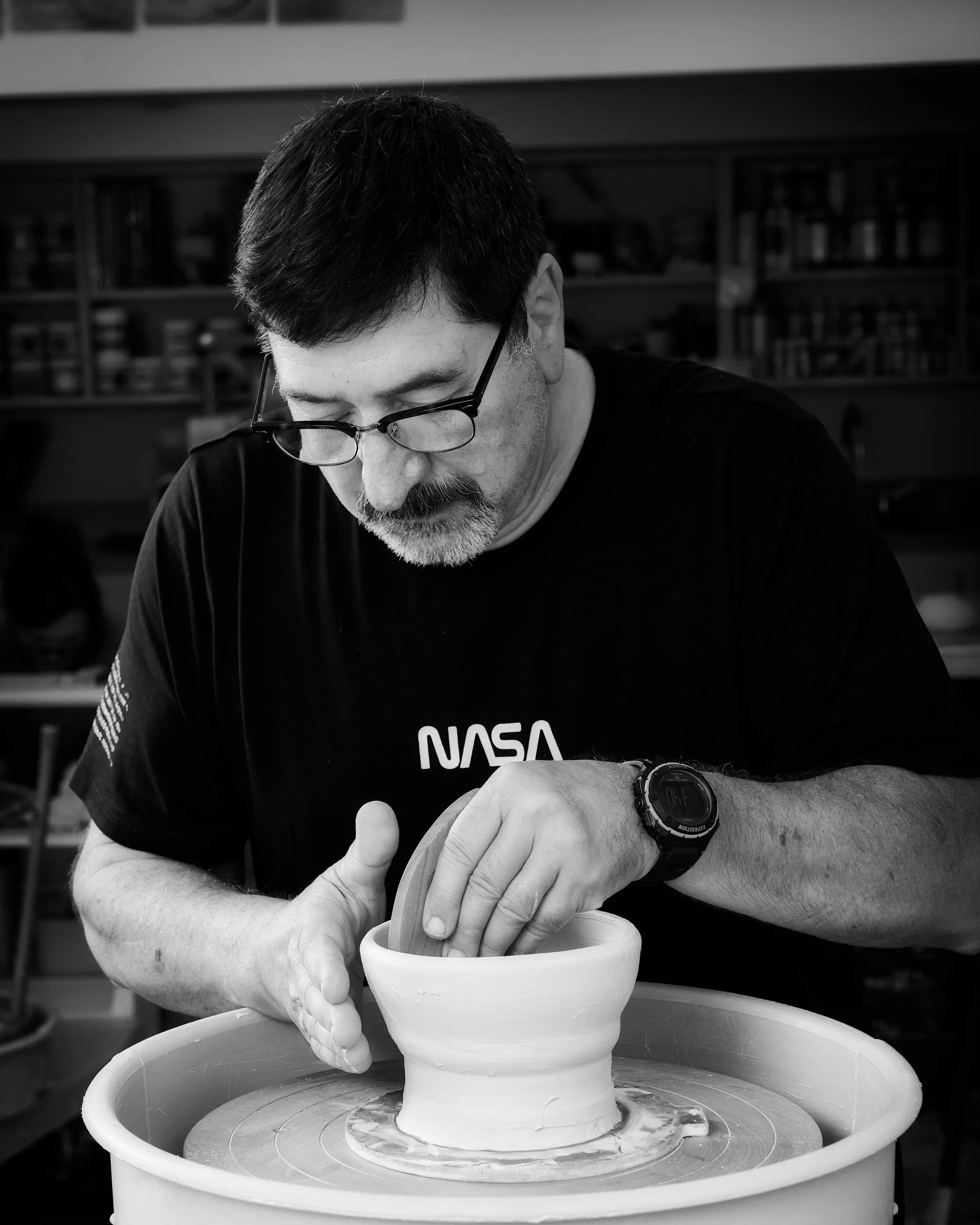 A man working on a ceramic piece on a pottery wheel in a studio.